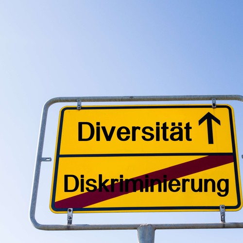 Das Bild zeigt ein Ortseingangsschild, auf dem es Richtung Diversität geht und Diskriminierung hinter sich gelassen wird. ©AdobeStock / pusteflower9