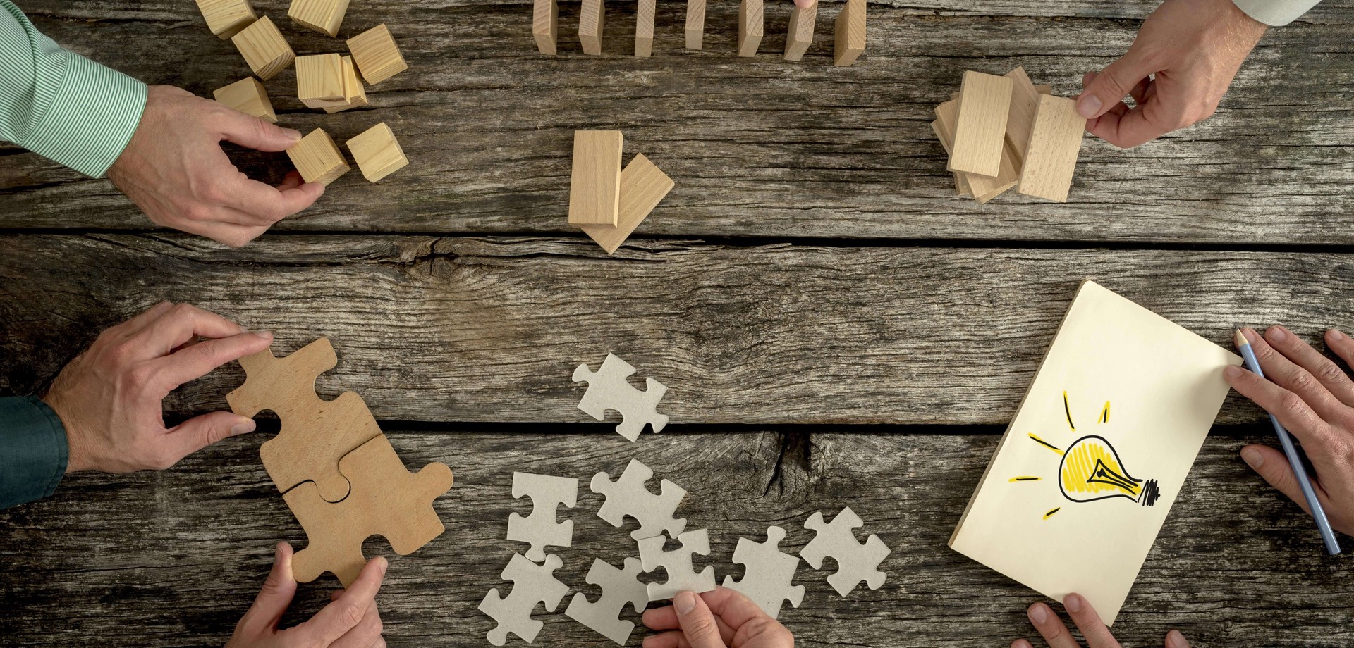 Das Bild zeigt Holzblöcke auf einem Tisch, die von mehreren Händen bewegt werden. ©AdobeStock / Gajus